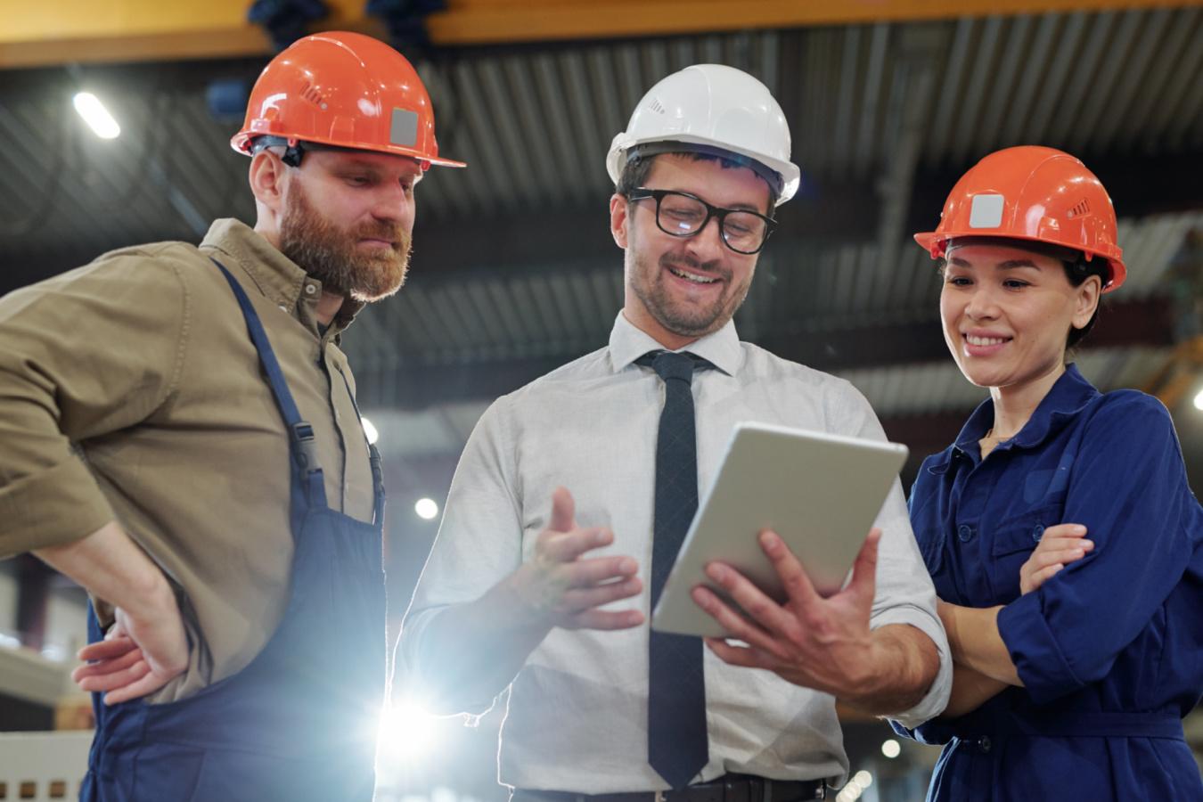 three factory workers looking at a tablet and smiling